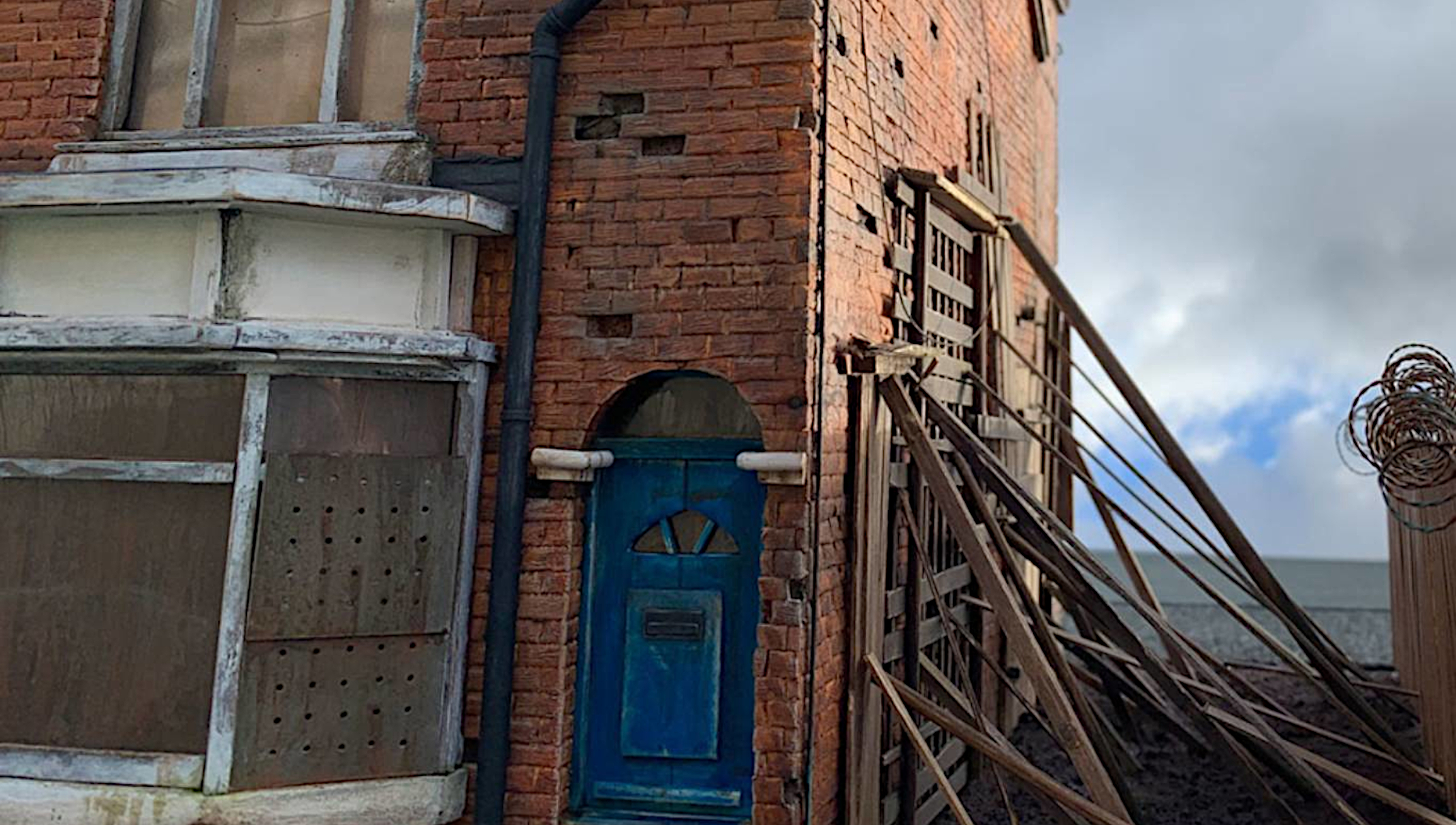 Detailed miniature red-brick building with a blue door and timber braces from Black Hole Redux by Dale Christopher Wells